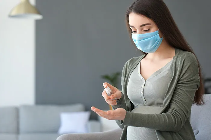 Grávida aplicando álcool gel na mão e usando máscara